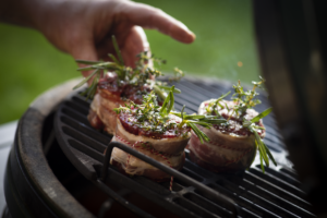 Big Green Egg Grill mit Filetsteaks im Speckmantel, verfeinert mit frischem Rosmarin und Thymian, beim direkten Grillen.