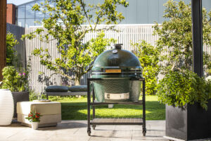 Big Green Egg Kamado-Grill auf fahrbarem Untergestell in einem modernen Gartenambiente.